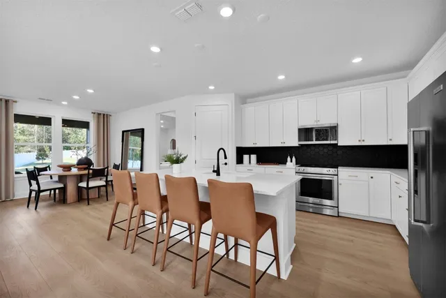 a kitchen with stainless steel appliances granite countertop a stove a sink a refrigerator a dining table and chairs with wooden floor