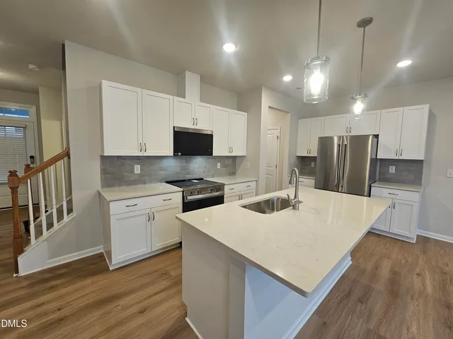 a kitchen with stainless steel appliances a stove top oven a sink a refrigerator white cabinets and wooden floor