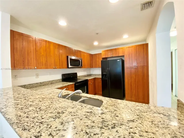 a kitchen with stainless steel appliances kitchen island granite countertop a refrigerator stove top oven and sink