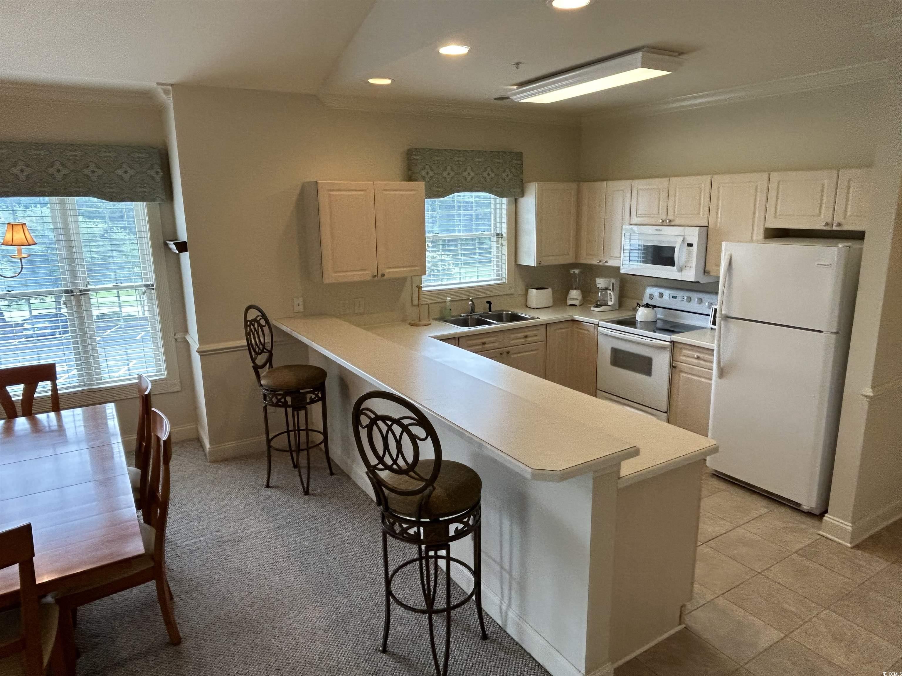 4893 Magnolia Pointe Lane, Unit 305 Myrtle Beach, SC 29577 - Photo 14 of 36 Kitchen with sink, white appliances, kitchen peninsula, and a breakfast bar area