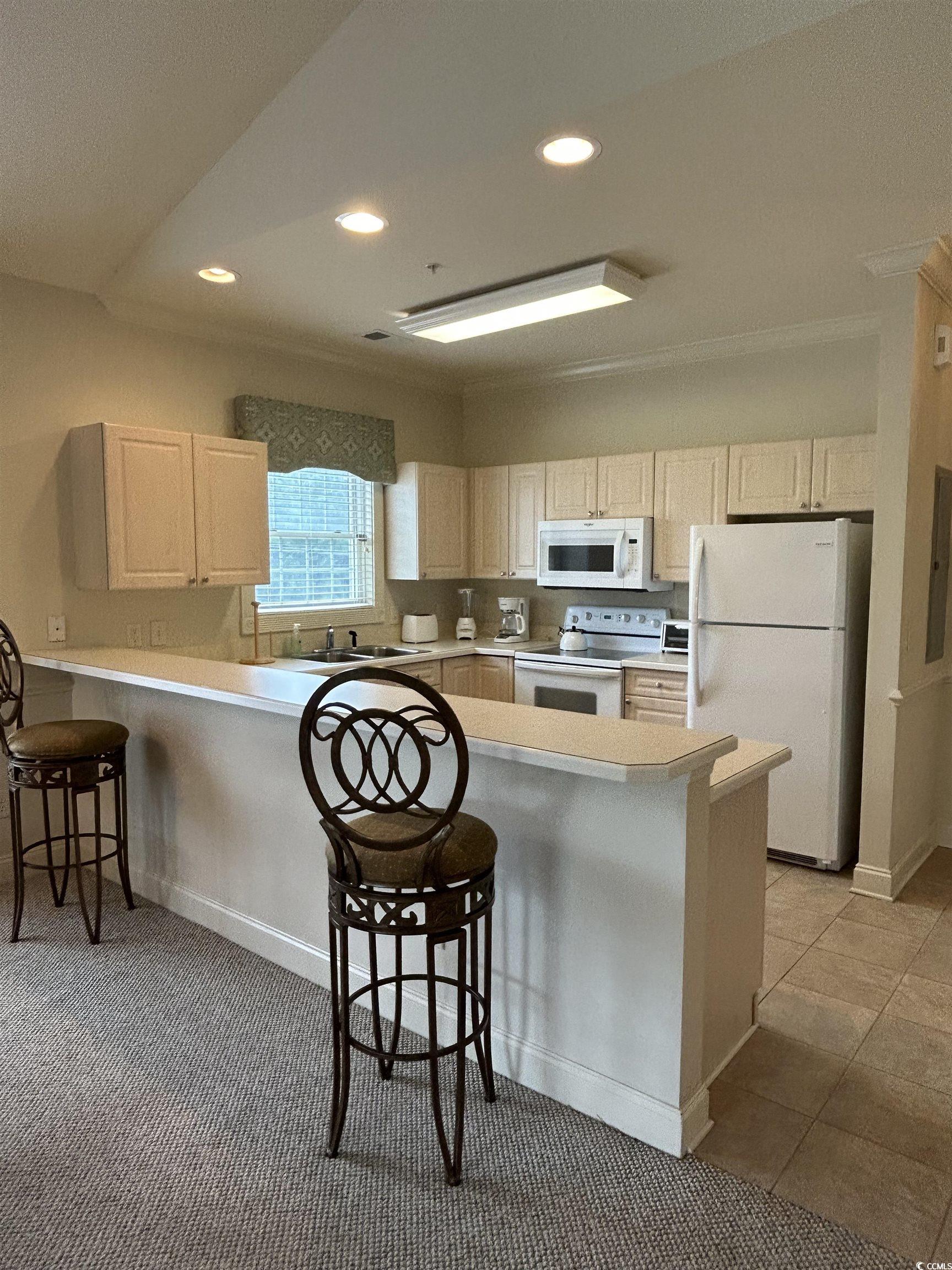 4893 Magnolia Pointe Lane, Unit 305 Myrtle Beach, SC 29577 - Photo 15 of 36 Kitchen with a kitchen bar, kitchen peninsula, white appliances, sink, and light tile patterned floors
