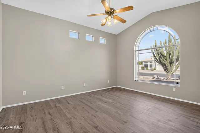 an empty room with wooden floor chandelier fan and windows