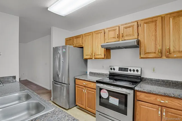 a kitchen with stainless steel appliances granite countertop a refrigerator a stove and a sink with wooden cabinets