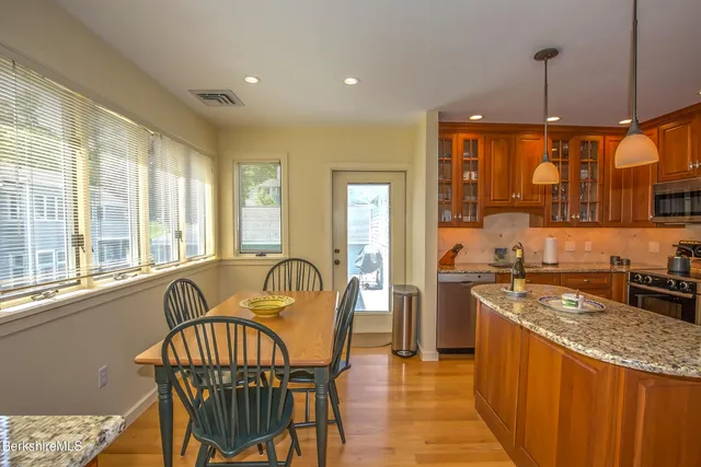 a kitchen with stainless steel appliances granite countertop a stove a sink a refrigerator a dining table and chairs