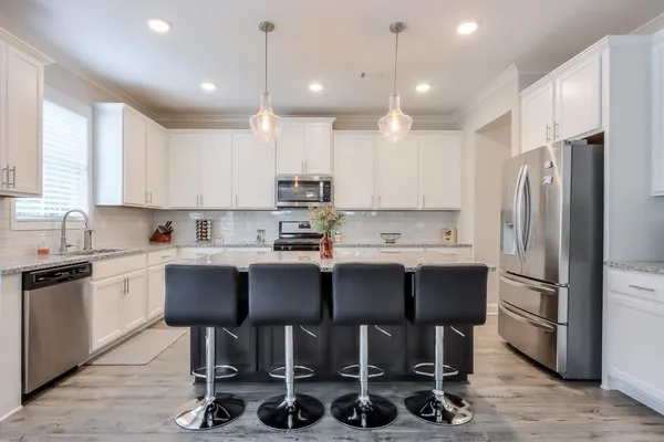 a kitchen with kitchen island granite countertop a table chairs refrigerator and microwave