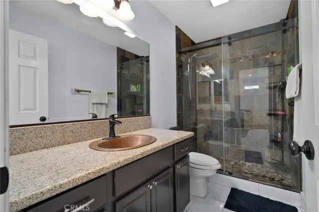 a bathroom with a granite countertop sink a toilet a mirror and shower