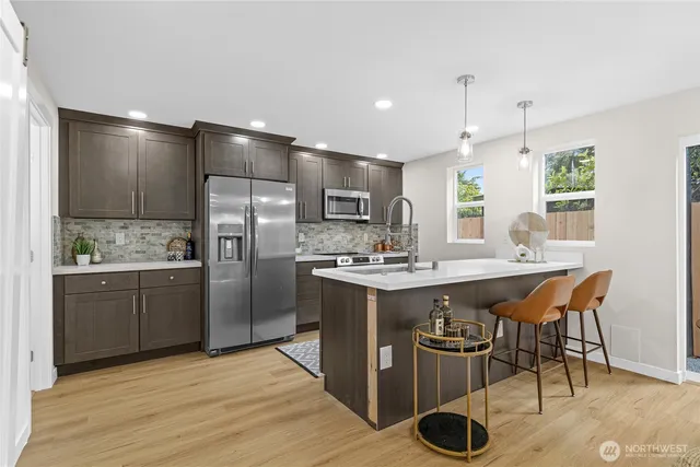 a kitchen with stainless steel appliances granite countertop a sink a stove a refrigerator and island with wooden floor