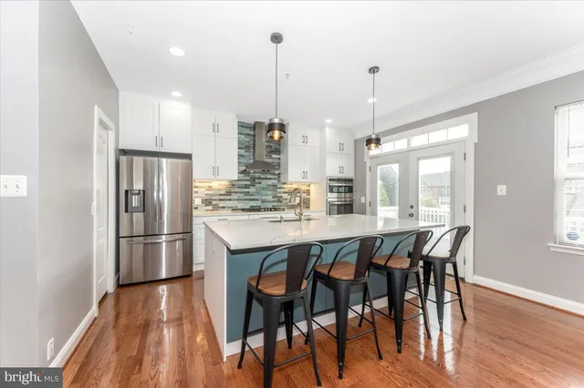 a kitchen with stainless steel appliances granite countertop a kitchen island a stove a refrigerator a sink a dining table and chairs with wooden floor