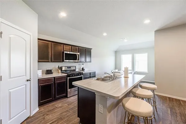 a kitchen with a stove a sink dishwasher a dining table and chairs with wooden floor