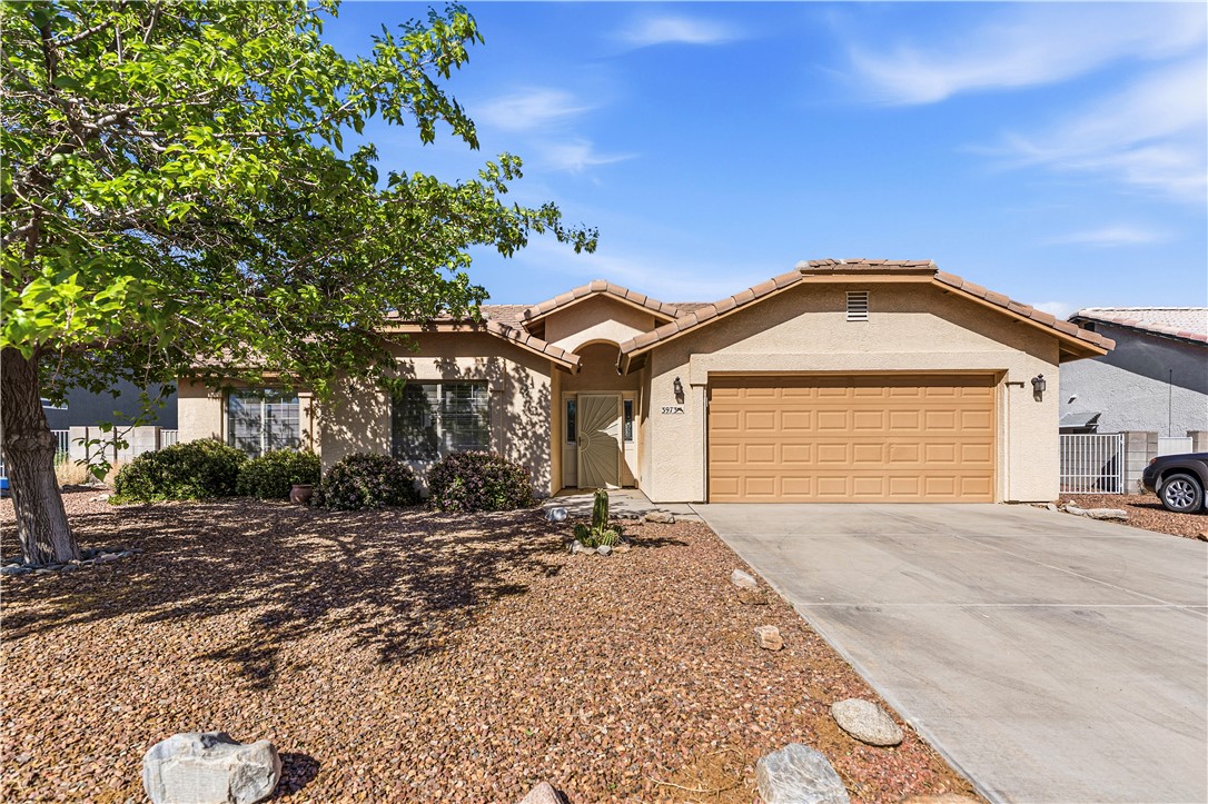 3973 Prairie View Drive Kingman, AZ 86409 - Photo 1 of 34 The property features a stucco exterior, an attached garage, a paved driveway, and a front yard with mature trees and desert landscaping