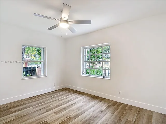 an empty room with wooden floor fan and windows