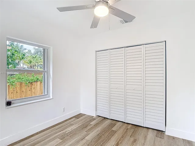 an empty room with wooden floor chandelier fan and windows