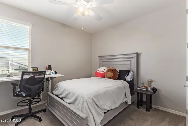 a bedroom with a bed a desk and chair with windows