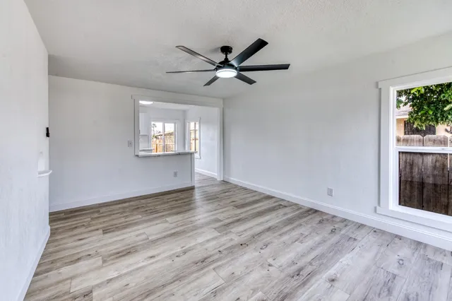 an empty room with wooden floor a ceiling fan and windows