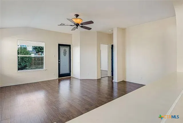 an empty room with wooden floor chandelier fan and windows