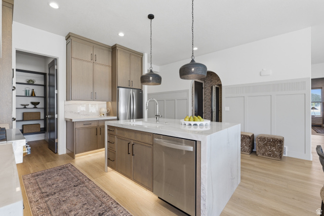 2559 West Aurora Avenue Mapleton, UT 84664 - Photo 8 of 60 Modern kitchen featuring a waterfall island with a stainless steel dishwasher, light wood-finish flooring, and two pendant lights
