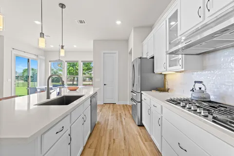 a kitchen with stainless steel appliances kitchen island granite countertop a sink a stove and a wooden floors