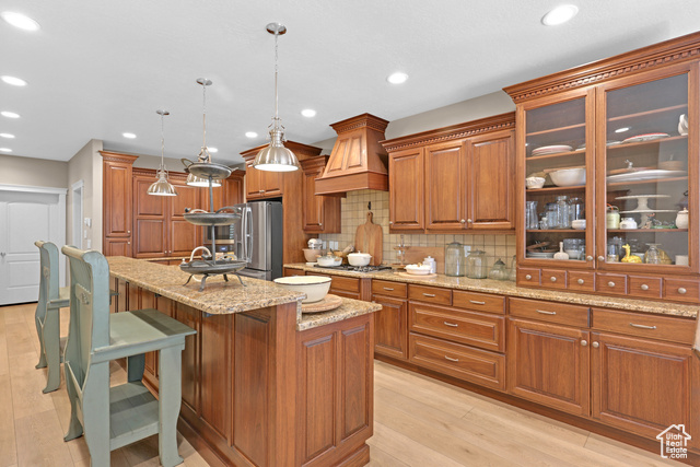 165 East 1550th South Perry, UT 84302 - Photo 15 of 26 Kitchen with decorative backsplash, a center island with sink, decorative light fixtures, custom exhaust hood, and light hardwood / wood-style floors