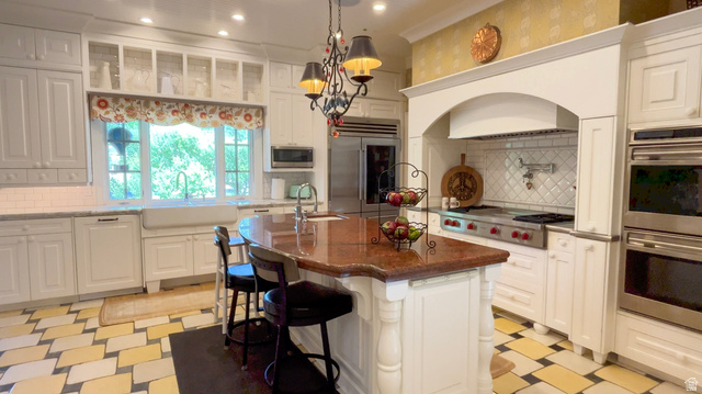 426 West Center Street Parowan, UT 84761 - Photo 14 of 107 White kitchen featuring a central island with a polished countertop, stainless steel appliances, a farmhouse sink, and a tiled backsplash
