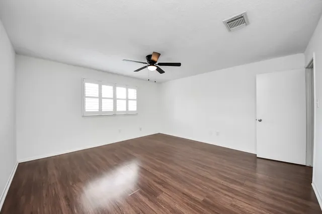 an empty room with wooden floor ceiling fan and windows