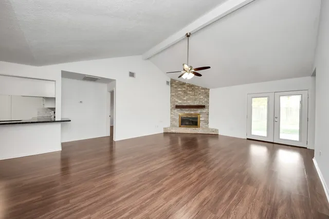 an empty room with wooden floor chandelier fan and windows