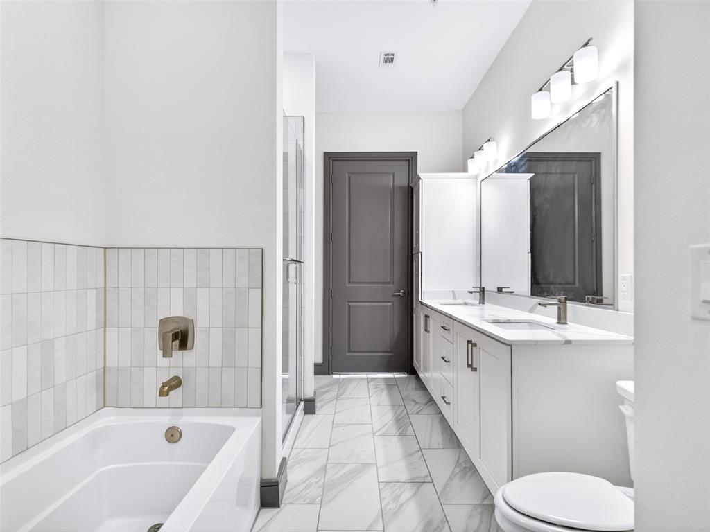 2700 Old Denton Road, Unit 4440 Carrollton, TX 75007 - Photo 29 of 32 Full bathroom featuring a single bathtub with brushed bronze fixtures, a glass-enclosed shower, a double vanity with undermount sinks and brushed nickel faucets, and marble-look tile flooring