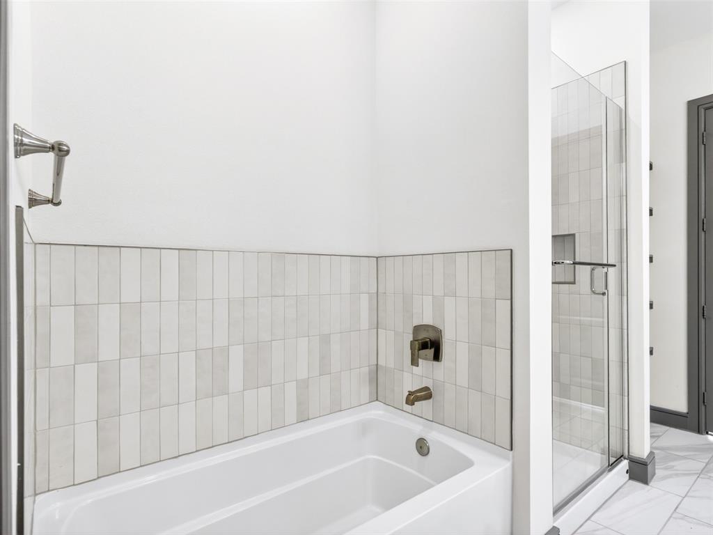 2700 Old Denton Road, Unit 4440 Carrollton, TX 75007 - Photo 30 of 32 Bathroom featuring a white soaking tub, vertical subway tile wainscoting, a bronze tub filler, a glass-enclosed shower, and a towel bar