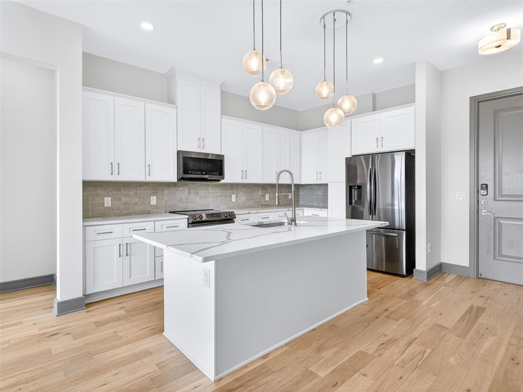 2700 Old Denton Road, Unit 4440 Carrollton, TX 75007 - Photo 3 of 32 Modern kitchen featuring white cabinetry, stainless steel appliances, a white island with an integrated sink, a tiled backsplash, and wood-finish flooring