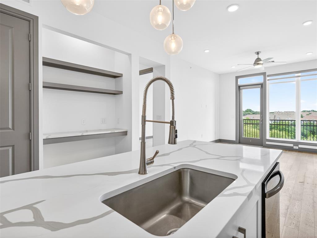 2700 Old Denton Road, Unit 4440 Carrollton, TX 75007 - Photo 5 of 32 Kitchen island featuring a stainless steel sink, gooseneck faucet, and white countertop with grey veining
