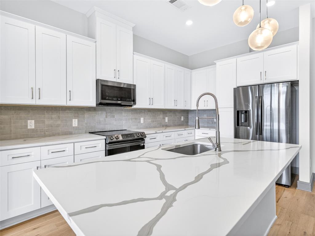 2700 Old Denton Road, Unit 4440 Carrollton, TX 75007 - Photo 7 of 32 Kitchen featuring a large central island with a waterfall edge and integrated sink, white cabinetry with contemporary hardware, stainless steel appliances, a gray subway tile backsplash, and wood-finish flooring