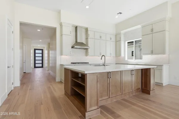 a large kitchen with stainless steel appliances a large counter top a sink dishwasher a refrigerator and white cabinets with wooden floor