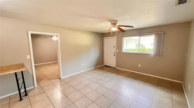 a view of an empty room with window and chandelier fan