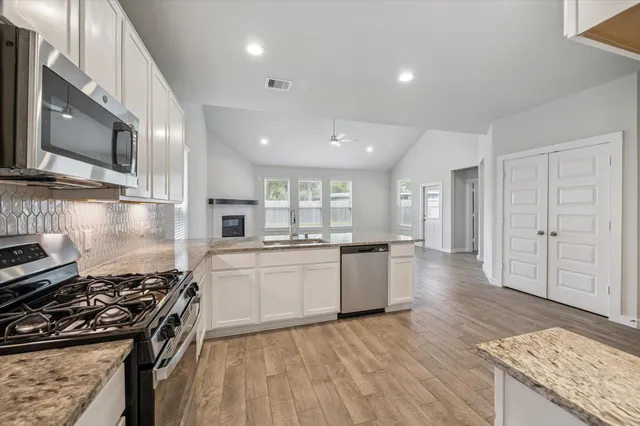 a kitchen with granite countertop a stove top oven a sink dishwasher and white cabinets with wooden floor