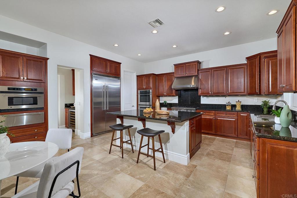 3230 Corte Aliso Carlsbad, CA 92009 - Photo 7 of 23 a kitchen with stainless steel appliances granite countertop a stove top oven a refrigerator a sink a dining table and chairs with wooden floor