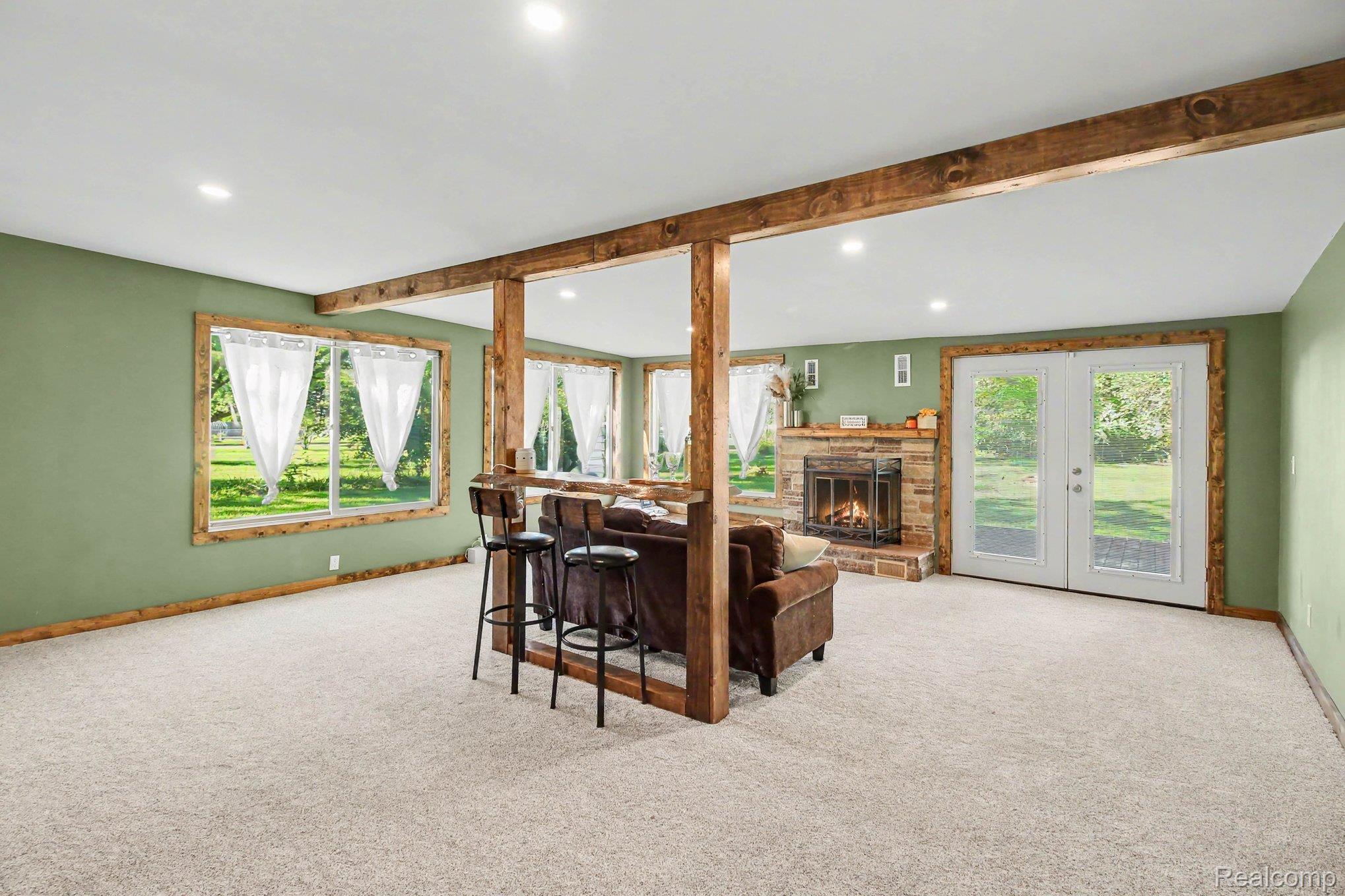 207 Elms Road Flushing, MI 48433 - Photo 12 of 30 Exposed wood beams and columns, recessed lighting, carpet flooring, stone fireplace with hearth, and double glass-panel doors
