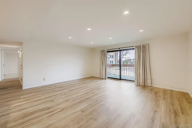 a view of an empty room with wooden floor and fan