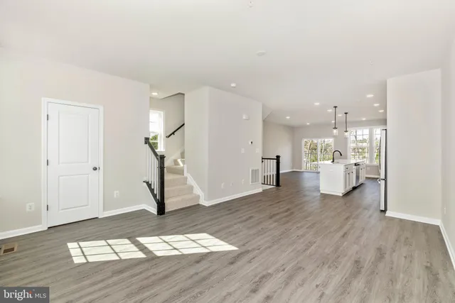 a view of an empty room and kitchen with wooden floor