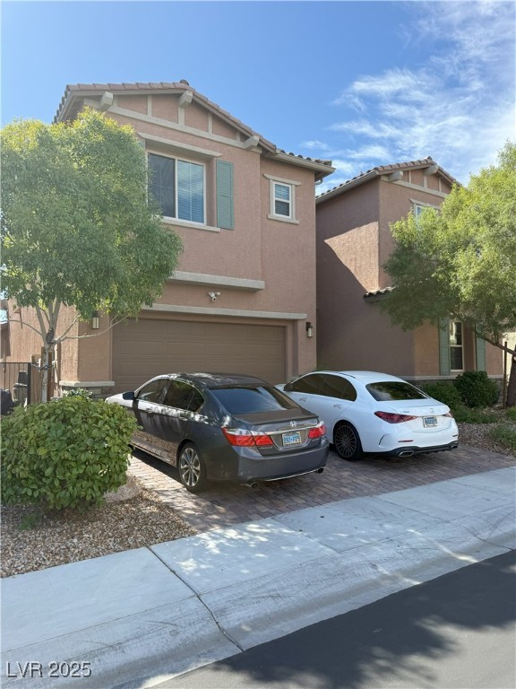 View of front of property with stucco siding, a tiled roof, driveway, and an attached garage