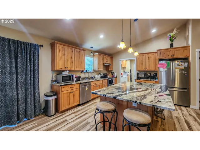 a kitchen with stainless steel appliances kitchen island granite countertop a sink refrigerator and cabinets