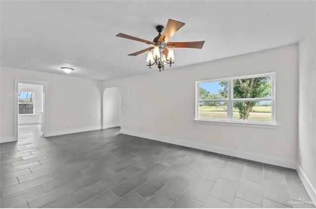 a view of an empty room with window and chandelier fan