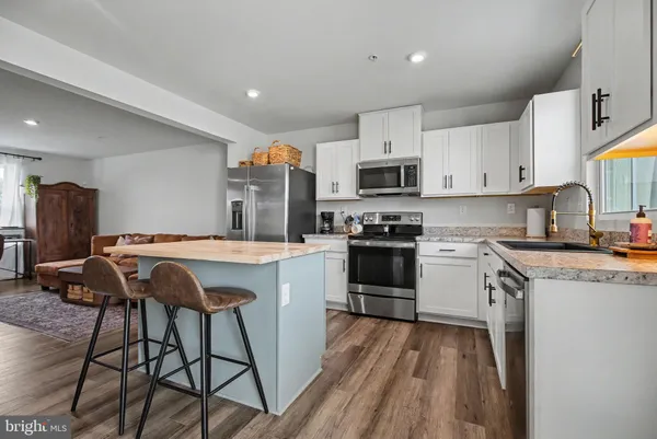 a kitchen with stainless steel appliances granite countertop a stove top oven a sink dishwasher and a refrigerator with wooden floor