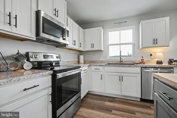 a kitchen with granite countertop white cabinets stainless steel appliances and a window
