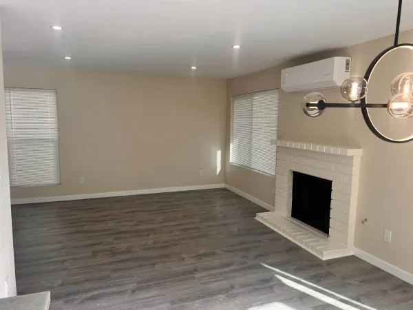 an empty room with wooden floor fireplace and windows