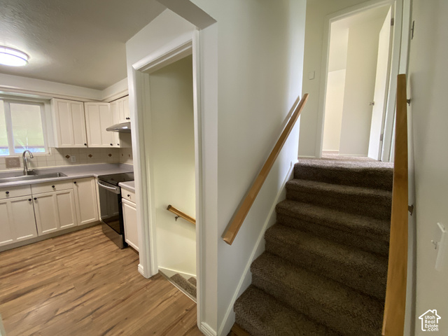 2989 Rae Street West Valley City, UT 84120 - Photo 9 of 25 Kitchen with wood-finish flooring, white cabinetry, integrated stainless steel appliances, and a tiled backsplash