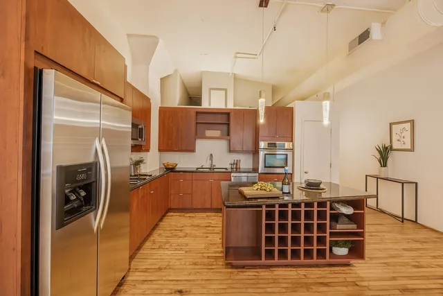 a large kitchen with stainless steel appliances a stove a refrigerator a oven with white cabinets and wooden floor