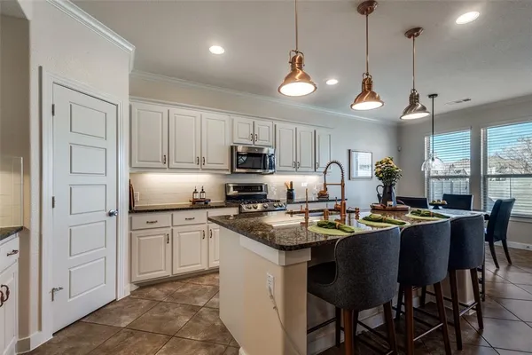 a kitchen with stainless steel appliances granite countertop a stove a refrigerator a sink a dining table and chairs