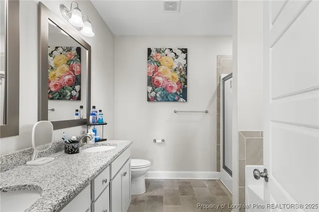a bathroom with a granite countertop sink a toilet and painting on the wall