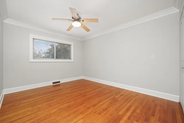 a view of an empty room with wooden floor and a ceiling fan