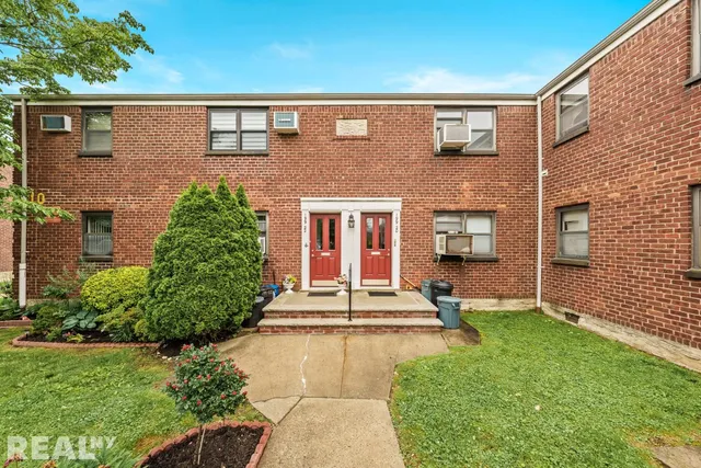 a view of a brick house with a large windows and a yard with plants and large trees