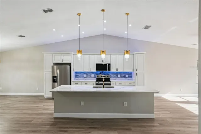 a kitchen with stainless steel appliances kitchen island granite countertop a refrigerator a stove top oven a sink dishwasher a refrigerator and white cabinets with wooden floor